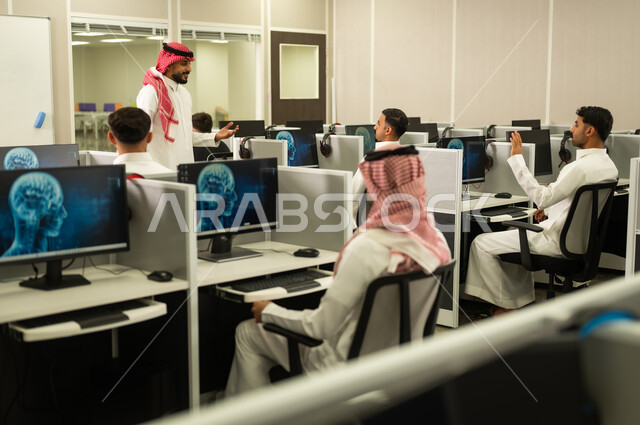 التعلم الرقمي للطلبة الجامعيين,  صورة من الخلف لمجموعه من الطلاب السعوديين يجلسون امام الكومبيوتر يستمعون الى شرح المعلم فى مختبر الحاسوب, تطوير أساليب التعليم الجامعي فى المملكة العربية السعودية