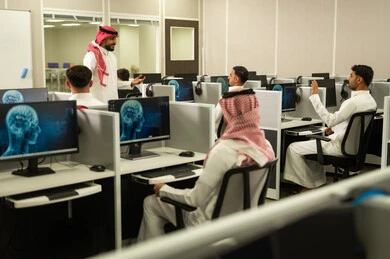 التعلم الرقمي للطلبة الجامعيين,  صورة من الخلف لمجموعه من الطلاب السعوديين يجلسون امام الكومبيوتر يستمعون الى شرح المعلم فى مختبر الحاسوب, تطوير أساليب التعليم الجامعي فى المملكة العربية السعودية