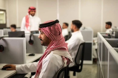 الحصص الدراسية عبر الكمبيوتر, مجموعة من الطلاب العرب الخليجيين السعوديين يجلسون فى مختبر حديث، التركيزعلى الدراسة والتفاعل الأكاديمي, موظف عربى خليجى سعودى يرتدى الثوب التقليدى والشماغ يعمل أمام جهاز الحاسوب