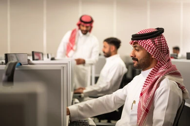 Practical application for students, education in the Kingdom of Saudi Arabia, an Arab Gulf Saudi employee wearing traditional thobe and shemagh working in front of a computer at the company headquarters, integration and focus at work
