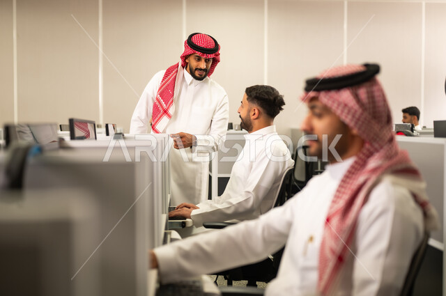 تبادل الأحاديث ضمن مقر الشركة، التعليم فى المملكة العربية السعودية,استخدام الأجهزة التقنية الحديثة معلم  يقوم بالشرح لطلابه, مجموعة من الموظفين العرب الخليجيين السعوديين يرتدون الثوب التقليدى يعملون أمام أجهزة الحاسوب في مقر الشركة