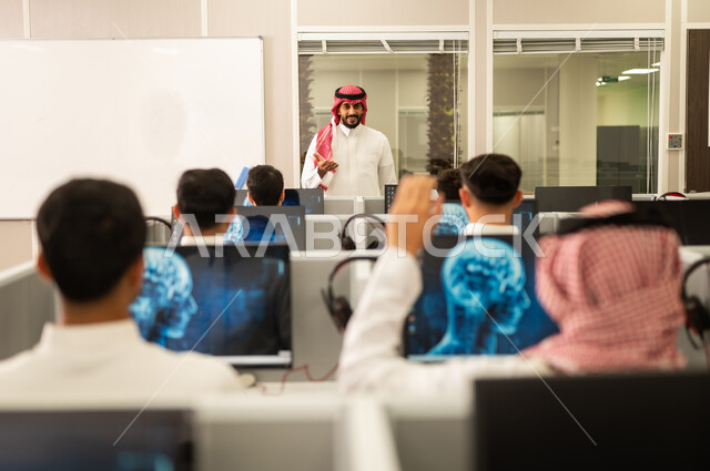 تصوير من الخلف لطلاب جامعة عرب سعووديين خليجيين فى مختبر كمبيوتر حديث. الدراسة و التعلم فى المملكة العربية السعودية. معلم سعودى يقوم بالشرح و التدريب على اجهزة الحاسوب