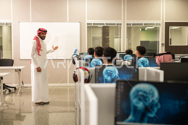 استخدام جهاز تقني حديث في التعلم والدراسة داخل الفصل الدراسي, مجموعة من الموظفين العربيين الخليجيين السعوديين يرتدون الثوب التقليدى يعملون أمام أجهزة الحاسوب في مقر الشركة, معلم عربي خليجي سعودى يقوم بشرح الدرس