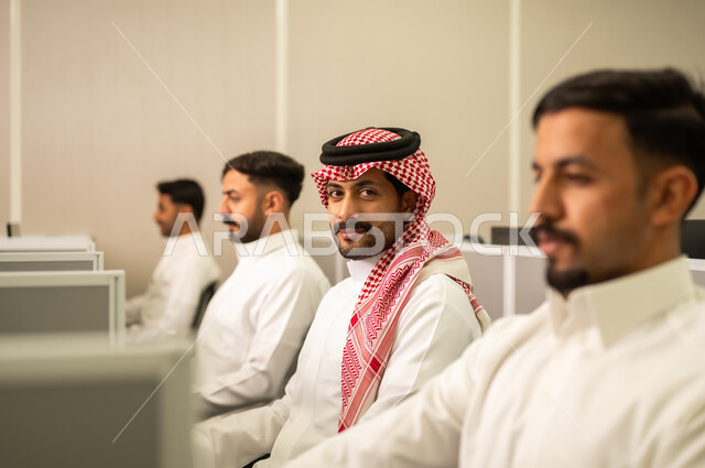 Workshops and training courses; an Arab Gulf Saudi employee wearing traditional attire works at a computer in the company headquarters; education in Saudi Arabia; Arab students sit at computers in the lab.