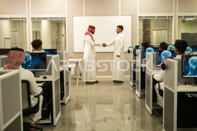 تبادل الخبرات والافكار، معلم عربي خليجي سعودي يرتدي الثوب التقليدي والشماغ يقوم بمناقشة الدروس مع طلابه, مجموعة من الموظفين العربيين الخليجيين السعوديين يرتدون الثوب التقليدى يعملون أمام أجهزة الحاسوب في مقر الشركة