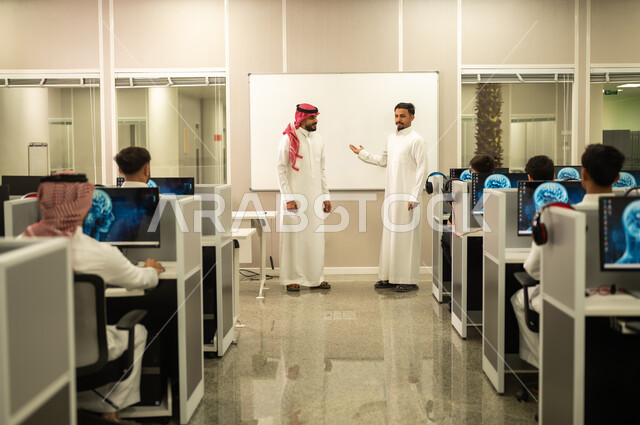 المشاركة والتعاون وتبادل الآراء بين زملاء العمل,  معلم عربي خليجي سعودي يرتدي الثوب التقليدي والشماغ يقوم بمناقشة الدروس مع طلابه, مجموعة من الموظفين العربيين الخليجيين السعوديين يرتدون الثوب التقليدى يعملون أمام أجهزة الحاسوب في مقر الشركة