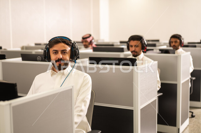 متابعة وتطوير العمل فى السعودية, مجموعة من الموظفين العربيين الخليجيين السعوديين يرتدون الثوب التقليدى يعملون أمام أجهزة الحاسوب في مقر الشركة, طلاب عرب يجلسون أمام أجهزة الكومبيوتر في مختبر حديث, استخدام تقنية الهيدفون