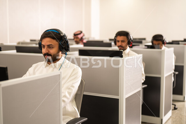 حل مشكلات العملاء عبر التواصل المباشر، مجموعة من الموظفين العربيين الخليجيين السعوديين يرتدون الثوب التقليدى يعملون أمام أجهزة الحاسوب في مقر الشركة, طلاب عرب يجلسون أمام أجهزة الكومبيوتر في مختبر حديث, استخدام تقنية الهيدفون