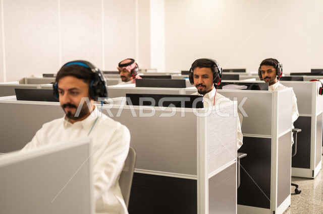Answering inquiries and questions; a group of Saudi Arabian Gulf employees wearing traditional attire work at computers in the company headquarters; excellence through diligence and perseverance; Arab students sit at computers in the lab; education in Saudi Arabia