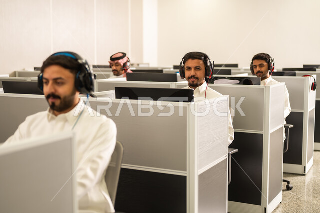 Enhancing customer satisfaction: A group of Saudi Arabian Gulf employees wearing traditional attire work at computers in the company headquarters. Excellence through diligence and perseverance: Arab students sit at computers in the lab. Education in Saudi Arabia.