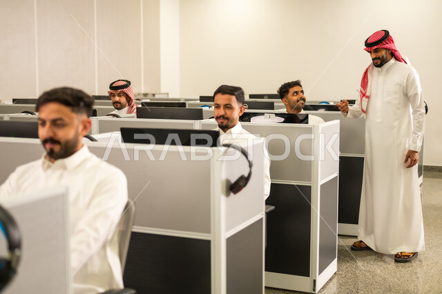 Colleague participation and collaboration; education in Saudi Arabia; Arab students sitting in front of computers in a modern lab; a group of Saudi Arabian Gulf employees wearing traditional attire working at computers in the company headquarters.