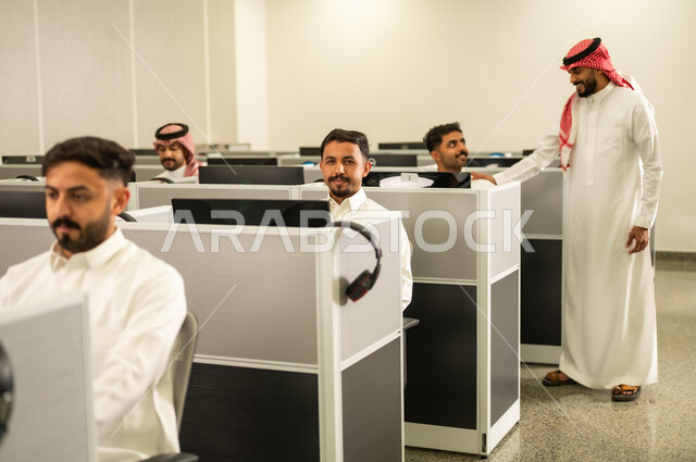 Excellence through diligence and perseverance: A group of Saudi Arabian students from the Gulf region, wearing traditional attire, sit in front of computers in a modern lab; e-learning within the classroom; A group of employees, also wearing traditional attire, work at computers in the company headquarters.
