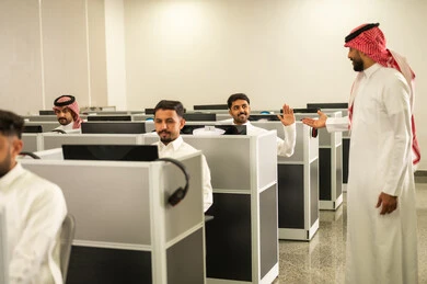 التعليم عبر الحاسوب الجامعي، مجموعة من الطلاب العرب الخليجيون السعوديون يرتدون الثوب التقليدى يجلسون أمام أجهزة الحاسوب في مختبر حديث,  مشاركة الطالب بواسطة رفع الايدي, التعليم في المملكة العربية السعودية