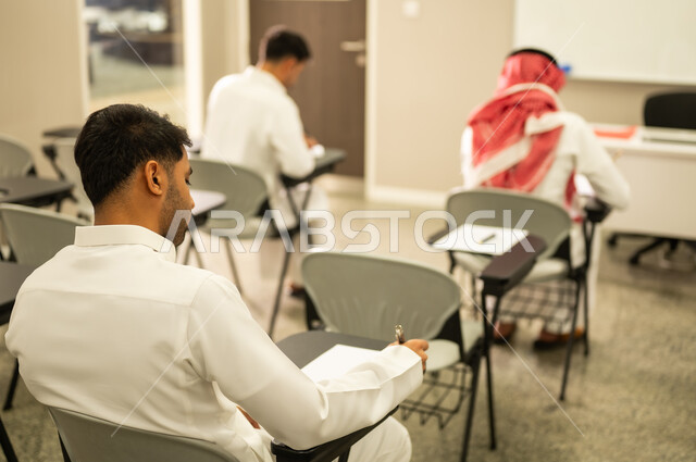 Diligence in studies to achieve success and academic excellence; a group of Saudi Arabian Gulf students solve exam questions with the help of their teacher; goals of education in the Kingdom of Saudi Arabia.