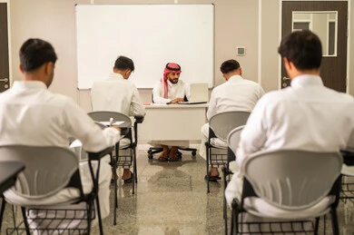 الشرح بدقة وايصال المعلومة للطلاب، معلم عربي خليجي سعودى يرتدي الثوب التقليدى و الشماغ يشرح درس للتلاميذ عن طريق الحاسوب ، التفاعل والنشاط والمشاركة داخل الفصل الدراسي