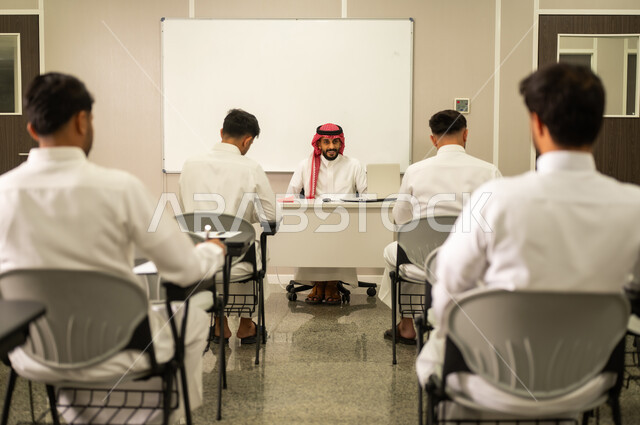 الارتقاء بالمعرفة العلمية ودعم الإبداع، متابعة مجموعة من الطلاب داخل الفصل، معلم عربي خليجي سعودى يرتدي الثوب التقليدى والشماغ  يشرح لطلابه في بيئه مدرسيه متطوره، نظام التعليم الحديث، جودة التعلم في المدارس الأكاديميه