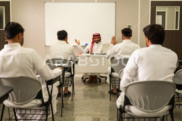 تعابير وايماءات الحماس لمعرفة الجواب الصحيح, طلاب عرب خليجيون سعوديون يقومون بحل أسئلة الاختبارات, معلم عربي خليجي سعودي يرتدي الثوب التقليدي والشماغ يقوم بمناقشة الدروس مع طلابه