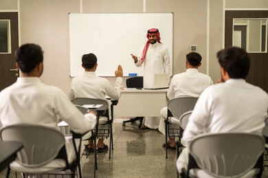 التربية والتعليم بالمناهج المقررة للطلاب في المملكة العربية السعودية, طلاب عرب خليجيون سعوديون يستمعون الى الدرس, معلم عربي خليجي سعودي يرتدي الثوب التقليدي والشماغ يقوم بمناقشة الدروس مع طلابه باستخدام الحاسوب