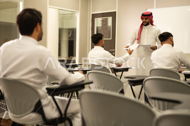 اجتهاد الطلاب لتحقيق التفوق، معلم عربي خليجي سعودي يقوم بتوزيع أوراق الامتحانات، متابعة الطلاب أثناء أداء الاختبارات، أهداف التربية والتعليم، التعليم بالمملكة العربية السعودية