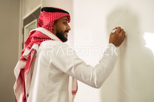 المقررات والمناهج التعليمية الحديثة والمطورة بالمملكة العربية السعودية, الاهتمام بقدرات الطلاب بتقديم الدروس, معلم عربي خليجي سعودي يرتدي الثوب التقليدي والشماغ يقوم بالشرح على اللوح الأبيض، استخدام السبورة لسهولة الشرح