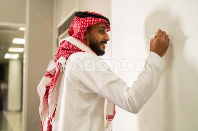 Educational goals, interaction and participation within the classroom, education in the Kingdom of Saudi Arabia, a Saudi Arabian Gulf teacher wearing a traditional thobe and shemagh explains the lesson to students using a whiteboard