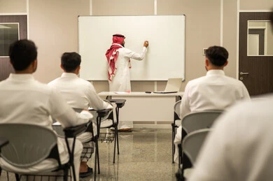 Active student participation; a Saudi Arabian teacher explains the lesson; a group of students interact in the class by listening attentively to the teacher; educational goals; classroom interaction; education in Saudi Arabia