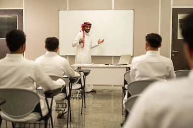 أهمية العلم في تنمية القدرات العقلية، المقررات و المناهج التعليمية في المملكة السعودية، صورة من الخلف لطلاب عرب خليجيين سعوديين يجلسون على المقعد المدرسى يستمعون الى استاذهم اثناء الدرس، ايماءات التركيز والتمعن بالدرس، استخدام اللوحة المدرسية البيضاء