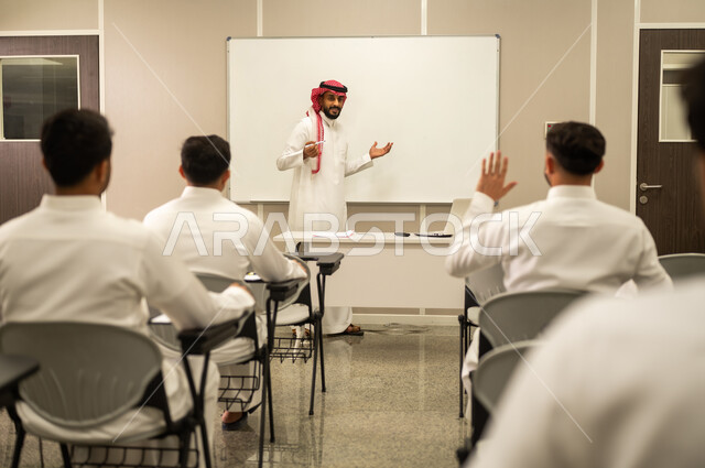 المشاركة الفعالة للطلاب, معلم عربي خليجي سعودي يقوم بشرح الدرس، مجموعة من الطلاب يتفاعلون في الحصة الدراسية من خلال رفع ايديهم للاجابة على اسئلة المدرس، المشاركة الفعالة للطلاب، أهداف التربية والتعليم، التفاعل والمشاركة داخل الفصل الدراسي، التعليم في السعودية