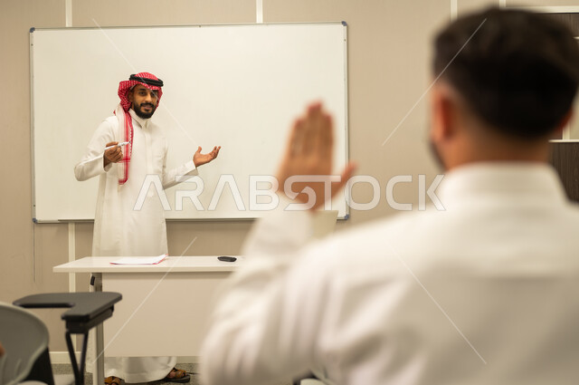 متابعة مجموعة من الطلاب داخل الفصل, معلم عربي خليجي سعودي يقوم بشرح الدرس, التفاعل والمشاركة داخل الفصل الدراسي, طالب عربى سعودى يتفاعل في الحصة الدراسية من خلال رفع يديه للاجابة على اسئلة المدرس، أهداف التربية والتعليم، التعليم في السعودية