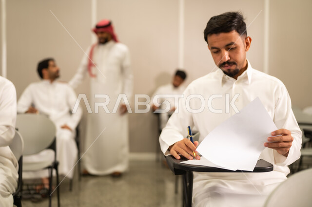 الاستعداد لحل أسئلة الامتحان , التربية والتعليم , المقررات والمناهج التعليمية الحديثة والمطورة في المملكة العربية السعودية, اختبارات نهاية الفصل الدراسي, طالب عربى خليجى سعودى يرتدى الثوب التقليدى يقوم بحل اسئلة الاختبار, التعليم في المملكة العربية السعودية, اهداف التربية و التعليم