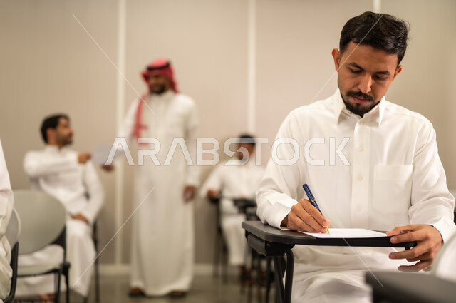 Participation, competition, and answering questions; modern and developed educational curricula and programs in the Kingdom of Saudi Arabia; end-of-semester exams; a Saudi Arabian student wearing traditional attire taking exam questions; education in the Kingdom of Saudi Arabia; educational goals.