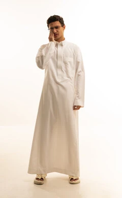 The concept of tooth decay, a portrait of a Gulf Arab Saudi man wearing traditional attire, holding his hand to his face with gestures of pain and toothache, swelling and inflammation in the mouth and gums, the necessity to see a doctor and get treatment, a full-body image, white background.