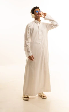 إيماءات الاندماج مع الأغنية، التفاعل مع الأنغام الموسيقية باستخدام الهيدفون،بورتريه لرجل عربي خليجي سعودي يرتدي الثوب التقليدي ونظارات طبية يستمع إلى الموسيقى من خلال سماعة الرأس بتعابير الانصات والاستمتاع، موهبة غنائية فنية، الجسم بالطول الكامل، خلفية بيضاء