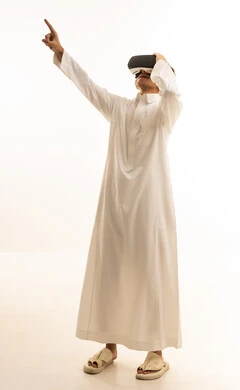 Simulation of the imaginary world, wearing virtual reality glasses, using modern technological devices, a portrait of a Saudi Arabian Gulf man wearing traditional attire and wearing 3D VR glasses, having a good time playing video games, white background.