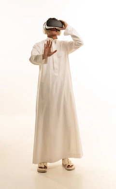 Wearing virtual reality glasses, simulating the imaginary world, using modern technological devices, a portrait of an Arab Gulf Saudi man wearing traditional attire and wearing 3D VR glasses, having a good time playing video games, white background.