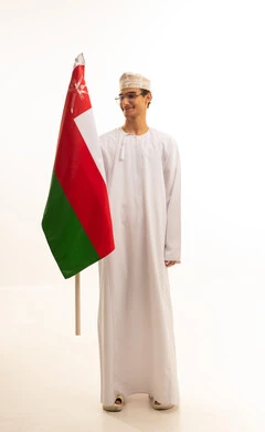 مفهوم حب الوطن والإنتماء إليه، ثقافات ورموز وطنية, الاعتزاز والفخر بالرموز والراية العمانية، الاحتفال بذكرى اليوم الوطني العماني، بورتريه لشاب عربي خليجي عماني يرتدي الدشداشة والكمة ونظارات طبية  يمسك بيده علم سلطنة عمان ، الجسم بالطول الكامل، خلفية بيضاء .