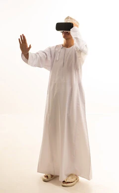 بورتريه لرجل عربي خليجي عماني يرتدي الدشداشة والكمة يضع نظارة الفي ار ثلاثية الأبعاد، قضاء وقت ممتع باللعب في العاب الفيديو ،محاكاة العالم الخيالي, ارتداء نظارات الواقع الافتراضي, استخدام الأجهزة التقنية الحديثة, خلفية بيضاء