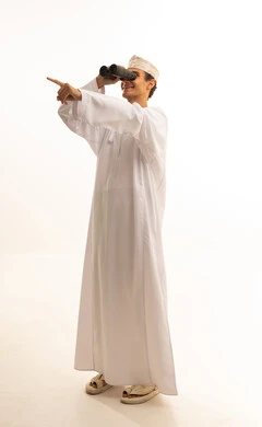 بورتريه لرجل عربي خليجي عماني يرتدي الدشداشة والكمة  ينظر من خلال منظار الرؤية ثنائي العينين, حب الاستكشاف والمغامرة، رؤية الاشياء البعيدة عبر التلسكوب بايماءات الاندهاش والسرور، التخطيط المستقبلي للأهداف والطموحات، خلفية بيضاء