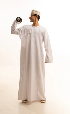 نشاط بدني للمحافظة على اللياقة الجسدية، رفع الأوزان الحديدية الثقيلة،بناء عضلات الجسم وتقويتها، بورتريه لرجل عربي خليجي عماني يرتدي الدشداشة والكمة ونظارات طبية يحمل الأثقال بيده ، خلفية بيضاء