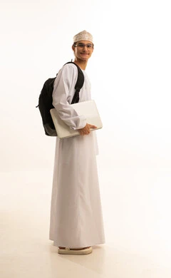 المواد والمناهج التعليمية في المملكة، مفهوم التعليم عن بعد، متابعة المحاضرات عبر المنصات التعليميه المتطوره، بورتريه لرجل عربي خليجي عماني يرتدي الدشداشة والكمة ونظارات طبية يضع حقيبة الظهر يمسك بيده جهاز اللابتوب، صورة لكامل الجسم، خلفية بيضاء