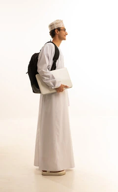 دمج التكنولوجيا المتطورة فى الحياة ، مفهوم التعليم عن بعد، المواد والمناهج التعليمية في المملكة، متابعة المحاضرات عبر المنصات التعليميه المتطوره، بورتريه لرجل عربي خليجي عماني يرتدي الدشداشة والكمة ونظارات طبية يضع حقيبة الظهر يمسك بيده جهاز اللابتوب، صورة لكامل الجسم، خلفية بيضاء