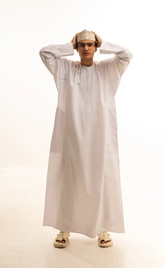 الشعور بالخيبة والانزعاج، إيماءات الحزن والإحباط، الندم على شيء ما، بورتريه لشاب عربي عماني يرتدي الدشداشة والكمة ونظارات طبية يضع يده على رأسه بتعابير العبوس, خلفية بيضاء