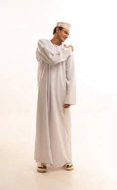 The need for treatment and seeking help, inflammation of the nerves, muscles, and joints, feeling sick and tired, a portrait of an Arab Gulf Omani man wearing a dishdasha and kumma and medical glasses, placing his hand on his shoulder with gestures of severe pain, white background.