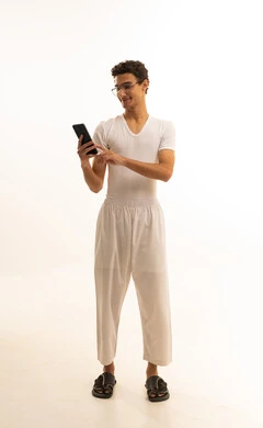 الدردشة مع الأصدقاء والأقارب عبر الجوال، ايماءات الفرح والسعادة، بورتريه لرجل عربي خليجي سعودي يرتدي السروال والفانيله البيضاء يمسك بيده الهاتف المحمول، دمج التكنولوجيا المتطورة الى الحياه اليومية، استخدام جهاز تقني حديث ومتطور، خلفية بيضاء