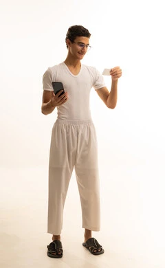 The ease of purchasing and paying via bank credit card, the ability to pay bills with electronic cards, a portrait of a Saudi Gulf Arab man wearing pants and a shirt holding a white card and working on a mobile phone, white background.