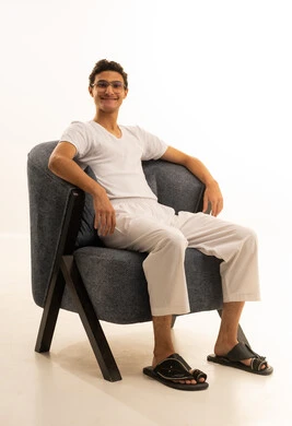 A portrait of a Saudi Arabian Gulf man wearing pants and a white t-shirt sitting on a comfortable chair looking at something with gestures of happiness, the concept of masculinity and elegance, attention to appearance, full-body, white background.