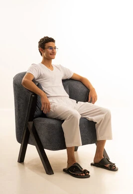 مفهوم الرجولة والأناقة، الاهتمام بالمظهر الخارجي، بورتريه لرجل عربي خليجي سعودي يرتدي السروال والفانيلة البيضاء يجلس على كرسي مريح ينظر الى شئ ما بايماءات السعادة ، الجسم بالطول الكامل، خلفية بيضاء