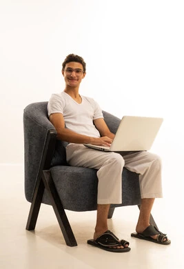 ادارة الأعمال عن بعد، استخدام الأجهزة الحديثة والمتطورة، بورتريه لرجل عربي خليجي سعودي يرتدي السروال والفانيله البيضاء يجلس على كرسي مريح يقوم باستخدام الحاسوب المحمول، دمج التكنولوجيا بالعمل، إنجاز المهام المطلوبة عبر اللابتوب، مهن ووظائف سعودية ، خلفية بيضاء