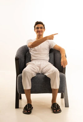 حركات تدل على هذا المكان (هنا), الدلالة على موقع معين, تحديد مكان عنصر محدد, بورتريه لرجل عربي خليجي سعودي يرتدي السروال والفانيله البيضاء يجلس على كرسي مريح يشير إلى شيء ما,  خلفية بيضاء