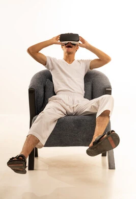 Simulation of the imaginary world, wearing virtual reality glasses, using modern technological devices, a portrait of a Saudi Arabian Gulf man wearing white pants and a t-shirt sitting on a comfortable chair wearing 3D VR glasses, having a good time playing video games, white background.
